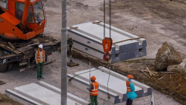 Installing concrete plates by crane at road construction site timelapse. Industrial workers with hardhats and uniform. Reconstruction of tram tracks in the city street. Aerial top view from above