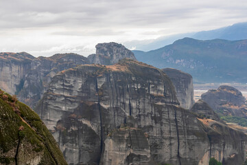 Naklejka premium Panoramic view of unique rock formations near Holy Monastery of Varlaam on cloudy foggy day in Kalambaka, Meteora, Thessaly, Greece, Europe. Rocks overgrown with green moss creating moody atmosphere