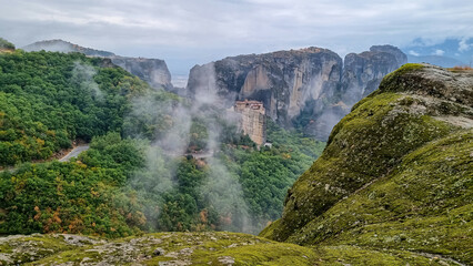 Road with scenic view of Holy Monastery of Rousanos appearing from the fog, Kalambaka, Meteora, Thessaly, Greece, Europe. Mystical atmosphere in dramatic landscape. Landmark build on rock formations