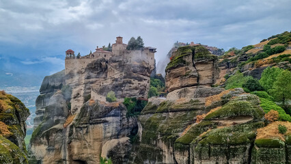 Scenic view of Holy Monastery of Varlaam on cloudy foggy day, Kalambaka, Meteora, Thessaly, Greece, Europe. Rock formations overgrown with green moss creating moody atmosphere. UNESCO World Heritage