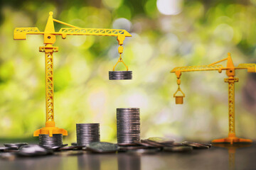 Construction cranes are stacking coins. business investment ideas - obrazy, fototapety, plakaty