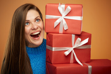 Happy woman in blue sweater holding stack of gift boxes and looking up. Isolated female portrait on orange background.