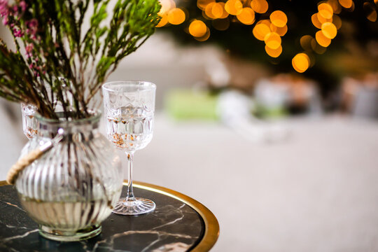 Cozy evening home interior - glasses, table, vase with a bouquet of Christmas tree branches against the background of Christmas lights. Horizontal photo