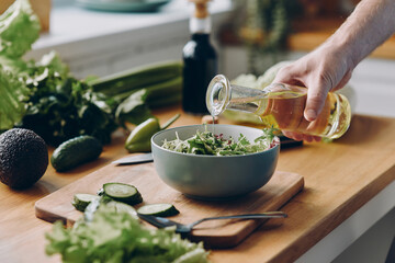 Close-up of unrecognizable man pouring olive oil into the bowl with fresh salad