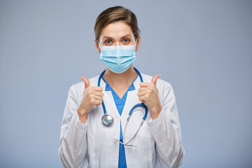 Smiling doctor woman with medical mask doing thumb up, isolated portrait.