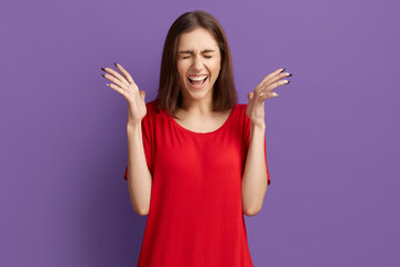 I cant believe in this. Pretty brunette girl in red t-shirt holding hands near face and squeal with pleasure. Closed her eyes, celebrate the victory. Posing over purple background. - obrazy, fototapety, plakaty