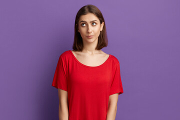 Oops, my bad. Confused pretty brunette girl in red t-shirt feeling awkward, lifting eyebrows and looking up. Looks very upset after making mistake and being guilty Posing over purple background.