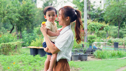 Asian young mother holding a playful little son in the park.
