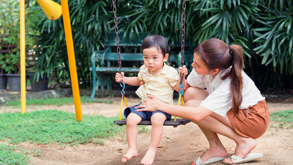 Mother taking her adorable little son sitting a swing.