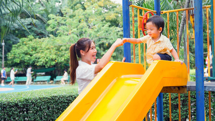 Mother encourage the little boy her by fist bump before the little son will play slides.
