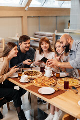 A group of friends is having pizza in a cozy restaurant and taking selfies, taking pictures together. A cheerful group of friends.