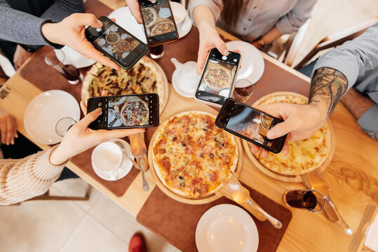 A cheerful group of friends takes pictures of delicious pizza in a restaurant. Friends are sitting in a restaurant and having fun.