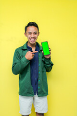 a man wearing a blue shirt with a green jacket and white pants making an expression with his smartphone, on a yellow background