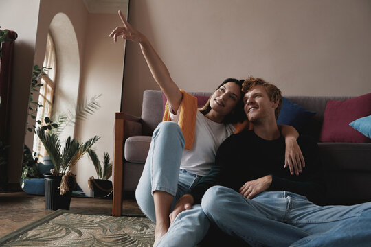 Beautiful young couple spending time at home together while woman pointing away and smiling