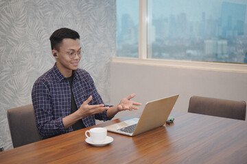 Video call. Asian man using laptop for video communication, man in glasses sitting at desk in modern office, looking at webcam and talking online