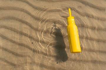A yellow bottle, thermos floating in the sea, ocean on sunny summer day. Symbol of summer, holidays and rest