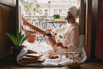 Fototapeta Beautiful young woman in bathrobe pouring champagne to the flute while relaxing on the balcony obraz