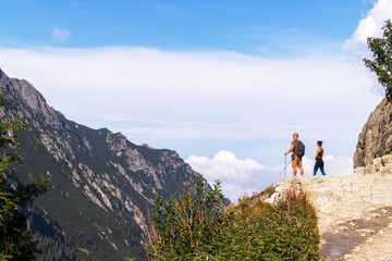 Obraz premium Beautiful landscape with mountains in the Polish Tatras with two people on the edge of the mountain and a very blue sky with white clouds