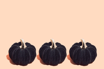 Three black decorative pumpkins on pastel beige background. Minimal autumn, Halloween or Thanksgiving composition