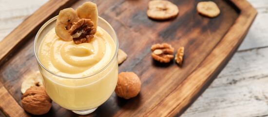 Glass of tasty pudding with banana and nuts on wooden background, closeup