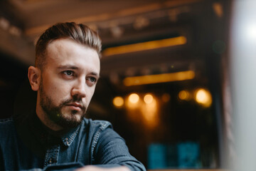 young male IT specialist with a beard and hairstyle works with a laptop in a cozy cafe. Online work on the Internet.