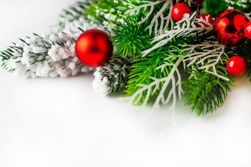 On a white background, fir branches with snow and red Christmas balls.