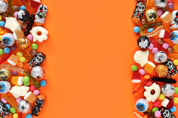 Halloween orange background with copy space in middle, assorted candies on both sides - traditional eyeballs chocolates, jelly worms, ghosts. Happy Halloween holiday sale and trick-or-treat concept.