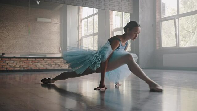 Graceful ballerina makes leg-split on floor stretching body