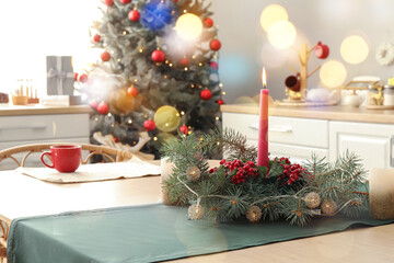 Burning candle with Christmas wreath on dining table in kitchen