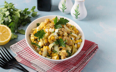 Salad with smoked fish, corn, onions and mustard in white bowl on light blue background