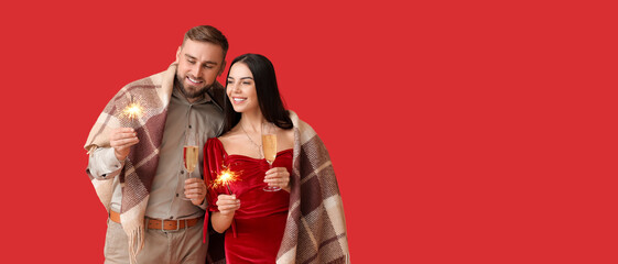 Happy young couple with Christmas sparklers and champagne on red background with space for text © Pixel-Shot