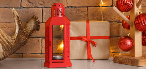 Lantern, gift and Christmas decor on table near brick wall