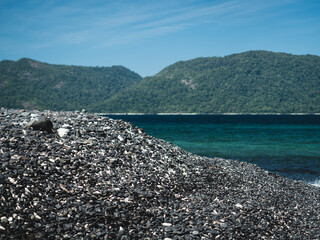 Scenic view of Koh Hin Ngam Island iconic black round pebble stone beach against turquoise sea. Near Koh Lipe Island, Tarutao, Satun, Thailand. Selective focus, blurred background.