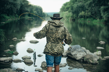 Back view of fisherman man on river or lake with fishing rod. Fishing hobby and spring weekend....