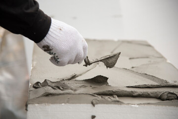 Close-up of worker hand, applying glue on white rigid polyurethane foam sheet. Thermal insulation...