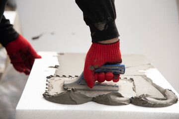 thermal insulation house. Close-up of worker hand, in red gloves with trowel applying glue on white...