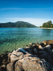 Scenic view of Sunset Beach, Koh Lipe Island. Crystal clear turquoise sea with coral reef transparent shallow water against Koh Adang Island background and rocky coastline foreground. Satun, Thailand.