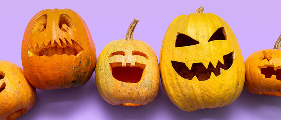Carved Halloween pumpkins on lilac background, top view