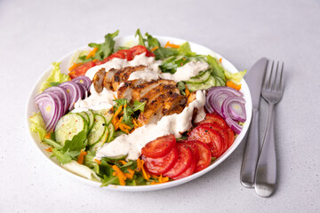 Warm salad with chicken, arugula, fresh vegetables and sour cream (yogurt) sauce. Home cooking, healthy food. White background, selective focus, close-up.
