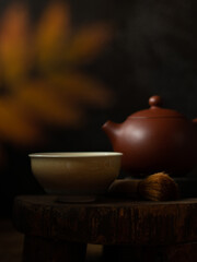 Chinese tea ceremony. Ceramic cup, yixing clay teapot, brush on a wooden tray looks like table. Defocused autumn leaf on a foreground