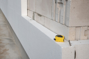 thermal insulation house. Black yellow tape measure on white rigid polyurethane foam sheet on wall.  - obrazy, fototapety, plakaty