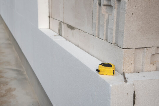 thermal insulation house. Black yellow tape measure on white rigid polyurethane foam sheet on wall. 