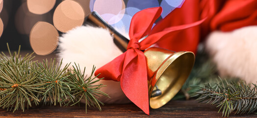 Golden Christmas bell and fir branches with Santa Claus hat on table against blurred lights