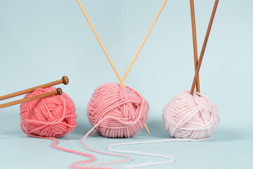Three yarn balls with wooden bamboo knitting needles on light blue background. Hobby, relaxation,...