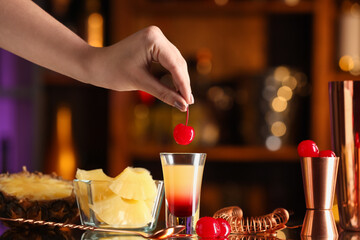 Bartender decorated tasty Pineapple Upside Down Cake cocktail with cherry on table in bar
