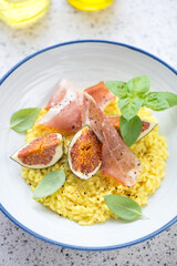 Close-up of risotto with cured ham, sliced fig fruits and green basil, vertical shot, selective focus