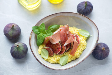 Bowl of risotto with fresh figs and prosciutto, high angle view on a light-grey granite background, horizontal shot