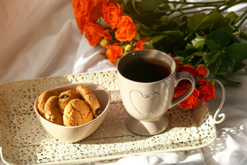 Cup of tasty coffee, cookies and bouquet of beautiful roses on bed