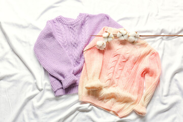 Children's sweaters and cotton flowers on white fabric background