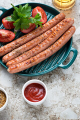 Green serving pan with grilled sausages, dips and beer on a light-brown granite background, vertical shot